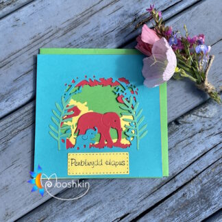 A layered, die cut greetings card featuring a mother and baby elephant walking in the forest