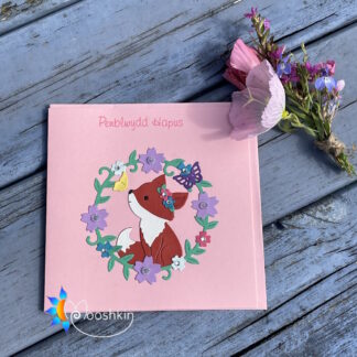 A handmade die cut pink greetings card featuring a fox cub surrounded by leaves, flowers and butterflies