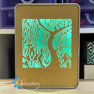 A Mooshkin Lantin featuring animals and trees die-cut into gold card, overlaid on green card, in a light-up scene inside a tin.