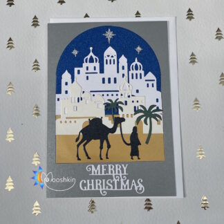 A handmade Christmas card featuring a man leading a camel in front of a middle-eastern town