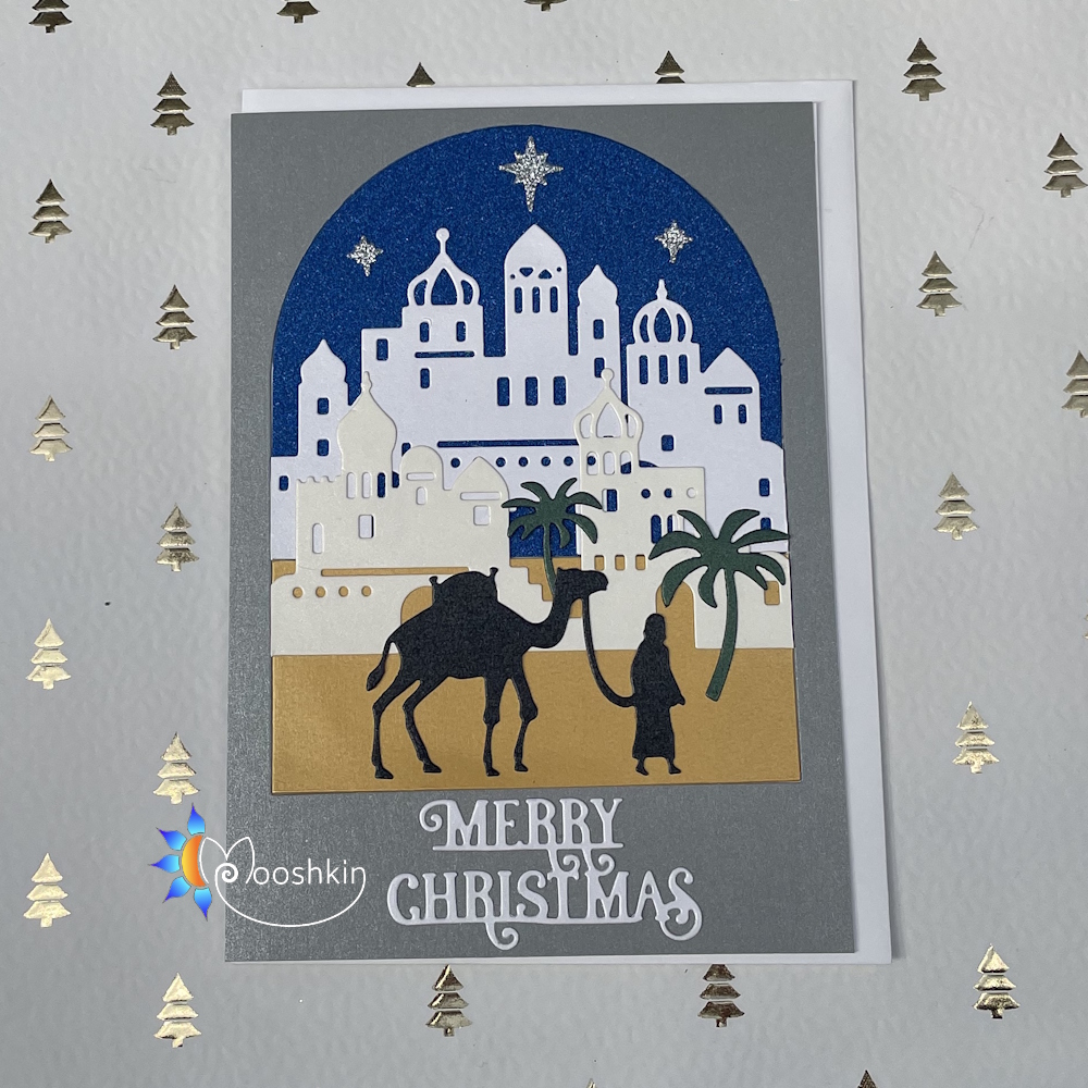 A handmade Christmas card featuring a man leading a camel in front of a middle-eastern town