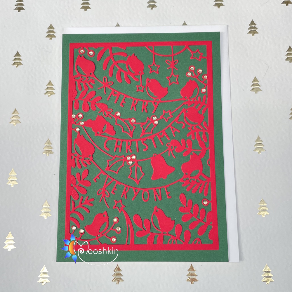 Handmade Christmas card: the message 'merry Christmas everyone' die cut into green card, on a red background, with birds, bells and wintry foliage