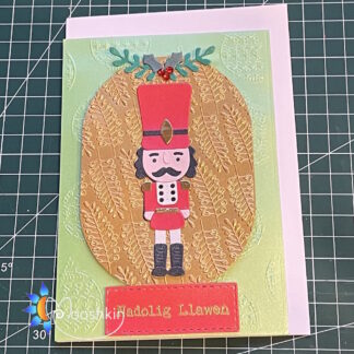 Handmade Christmas card: die cut nutcracker character in red uniform, on textured gold background